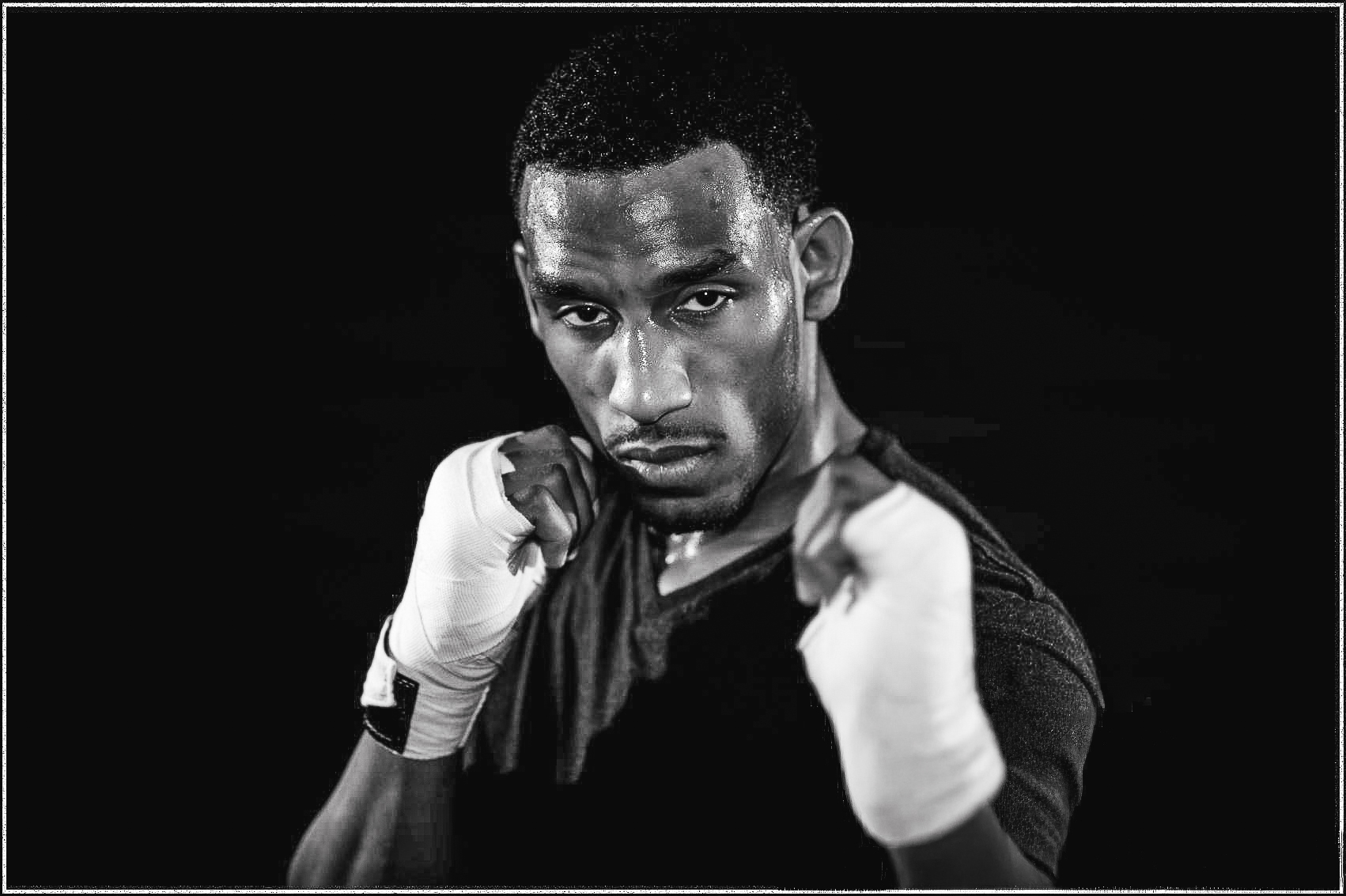 A real boxer stands in a defensive stance after sparring, wearing hand wraps and lit with dramatic split lighting against a dark background.