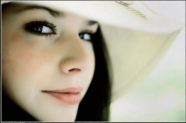 Close up portrait of a young woman wearing a white hat, looking softly to one side with a relaxed smile, photographed using natural light and a shallow depth of field.